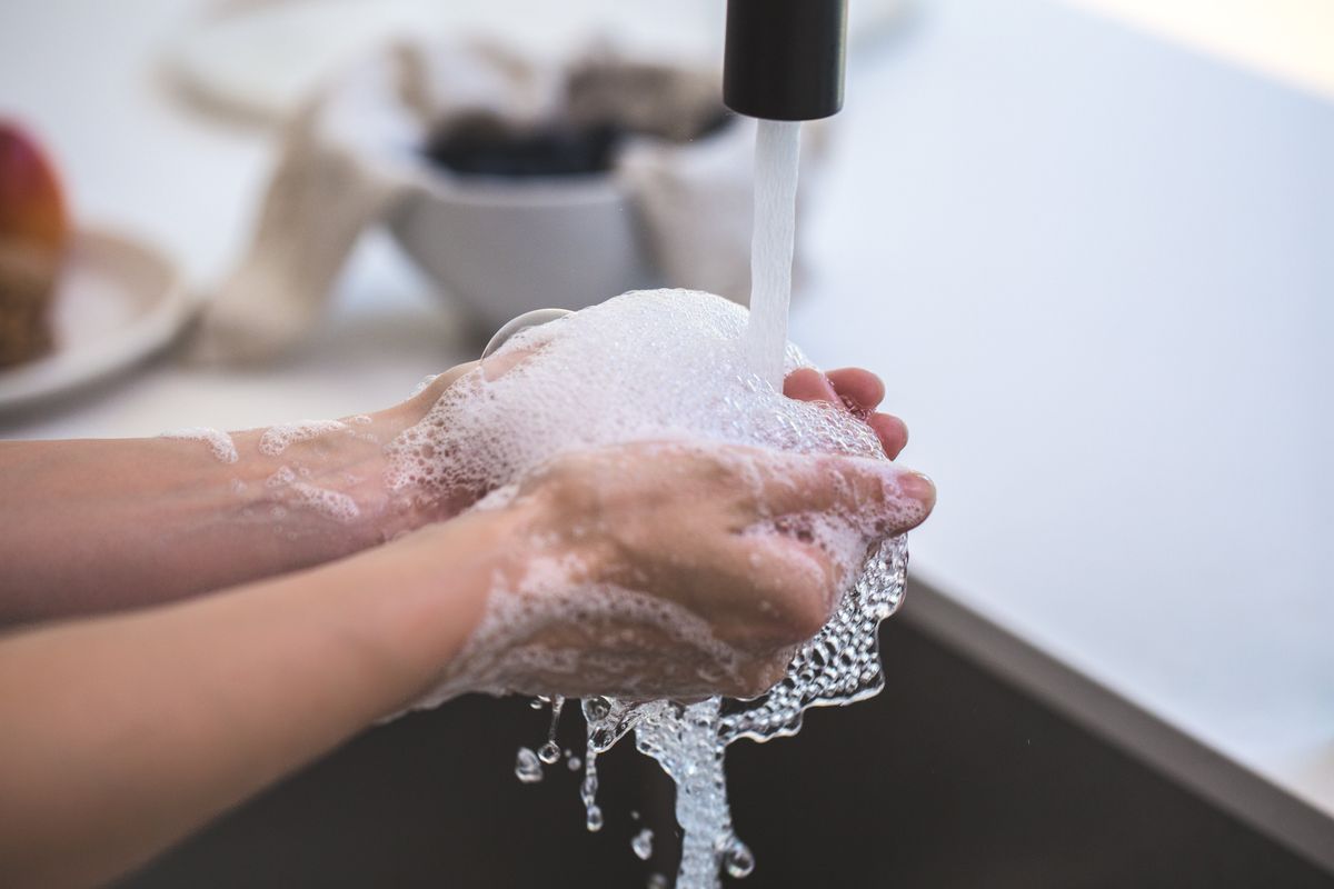 Hands being washed under a running faucet with abundant foam, illustrating how little product soft water needs