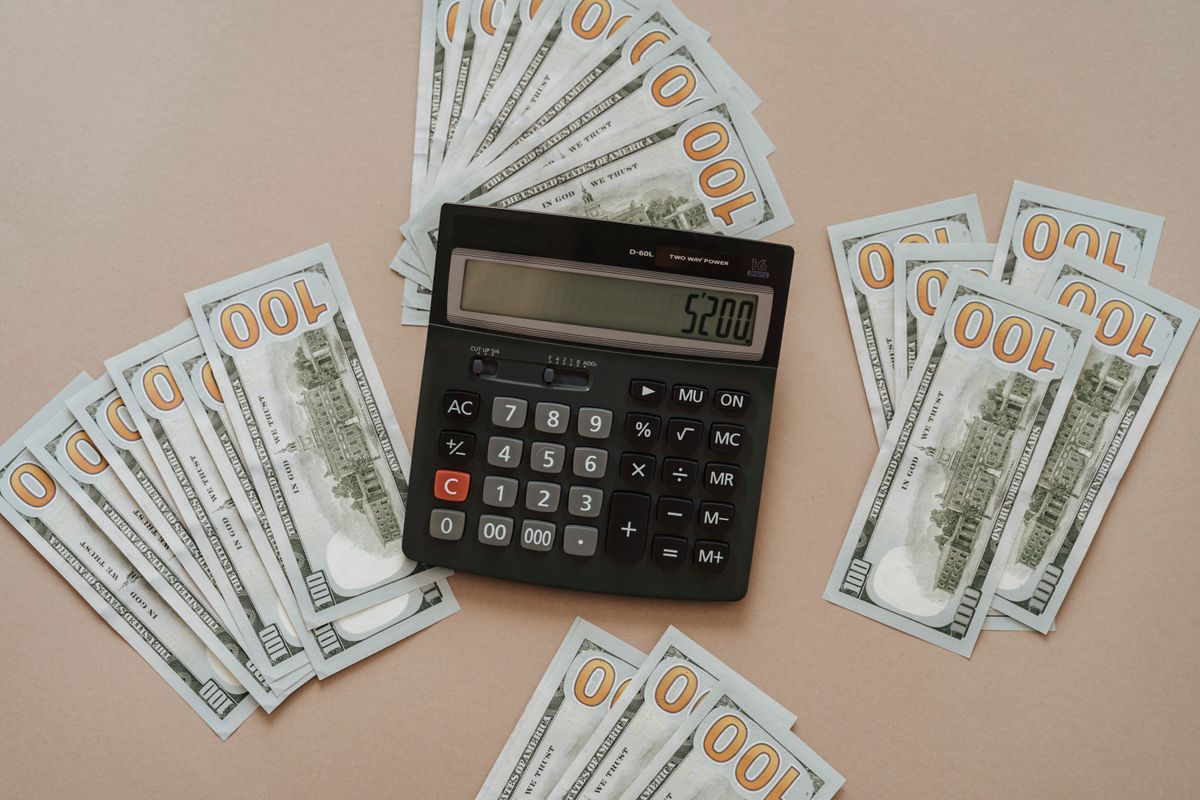 Black calculator showing 5200 lying among fanned hundred-dollar bills, the size of premium a Kinetico water softener quote can carry over an online twin-tank system