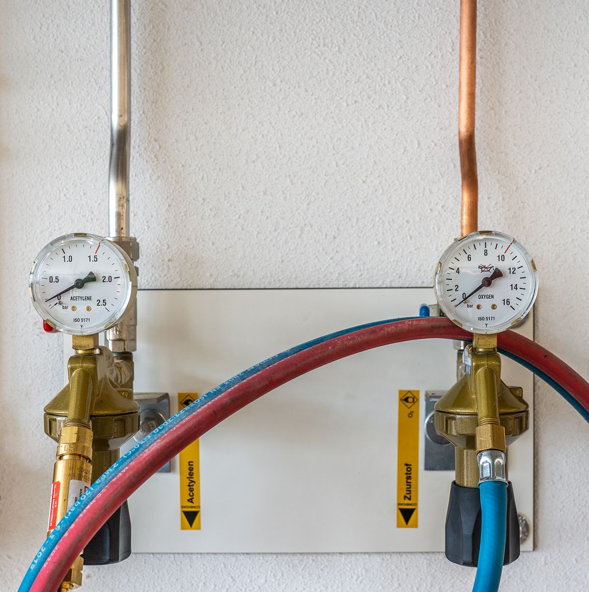 Two gas pressure gauges connected by hoses against a white wall, the same principle as fitting test gauges on the inlet and outlet side of a water softener