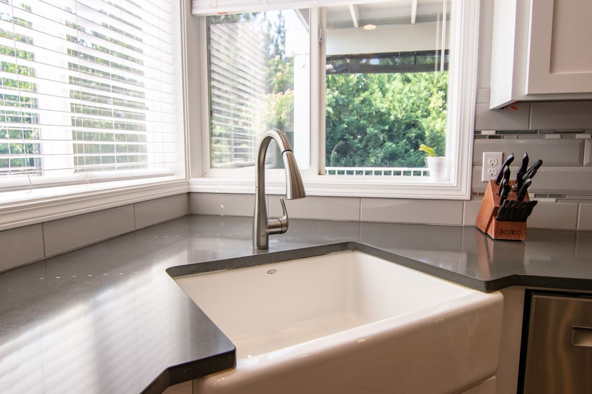 White farmhouse kitchen sink with a brushed nickel pull-down faucet under a bright window, one of the daily draws a softener's reserve has to cover