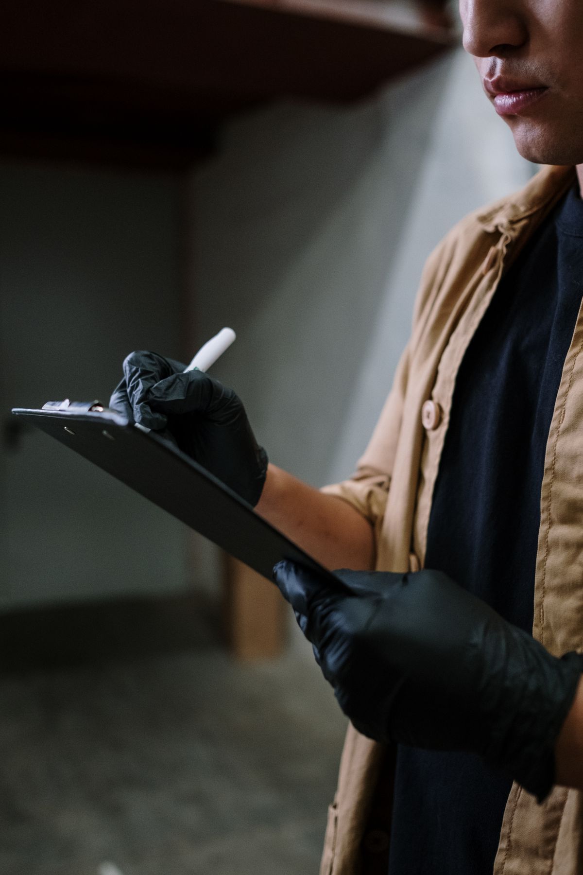 Service worker in black nitrile gloves writing on a clipboard checklist during a site visit