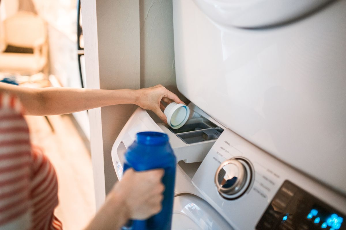 Person pouring liquid detergent into a washing machine dispenser drawer
