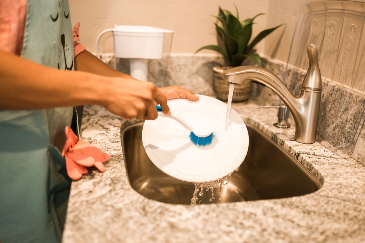 Person washing a plate under a running kitchen tap on city water, the supply a Watts OneFlow Plus salt-free system with carbon filtration is designed to treat