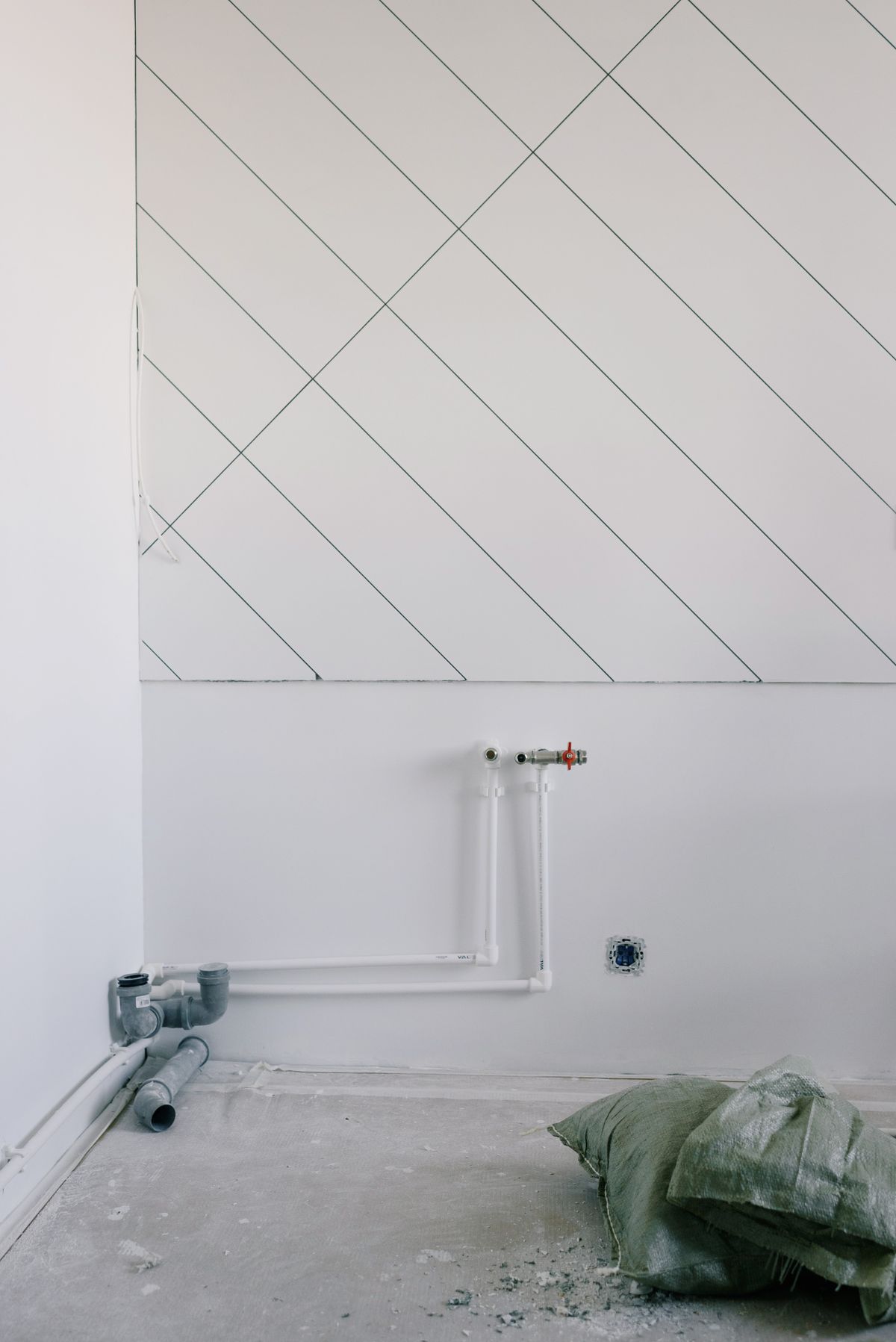 White plastic water supply pipes with a shut-off valve on a bare wall during a renovation, the cold main where a salt-free water conditioner is plumbed in
