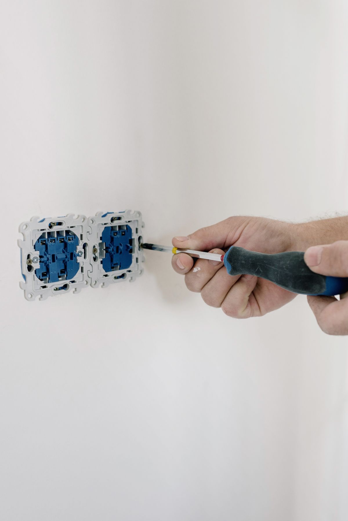 Electrician's hand using a screwdriver on a wall receptacle, the kind of outlet and control component that has to be replaced once floodwater has covered it