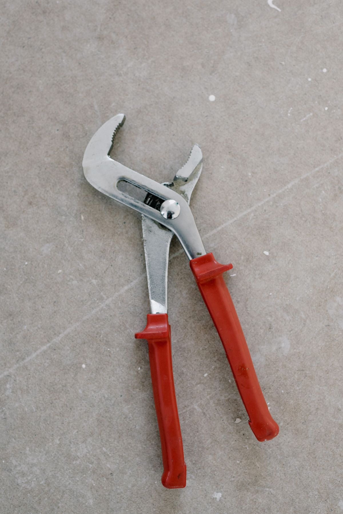 Red-handled tongue-and-groove plumbing pliers on a concrete floor, the kind of basic tool a DIY install of a SpringWell salt-based water softener needs