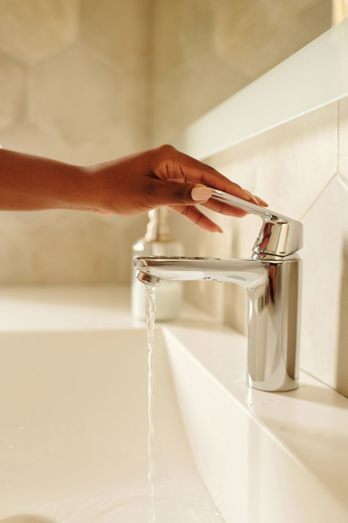 Hand lifting a chrome bathroom faucet lever as water runs into the basin, the uninterrupted soft water a twin-tank Kinetico softener supplies even while regenerating