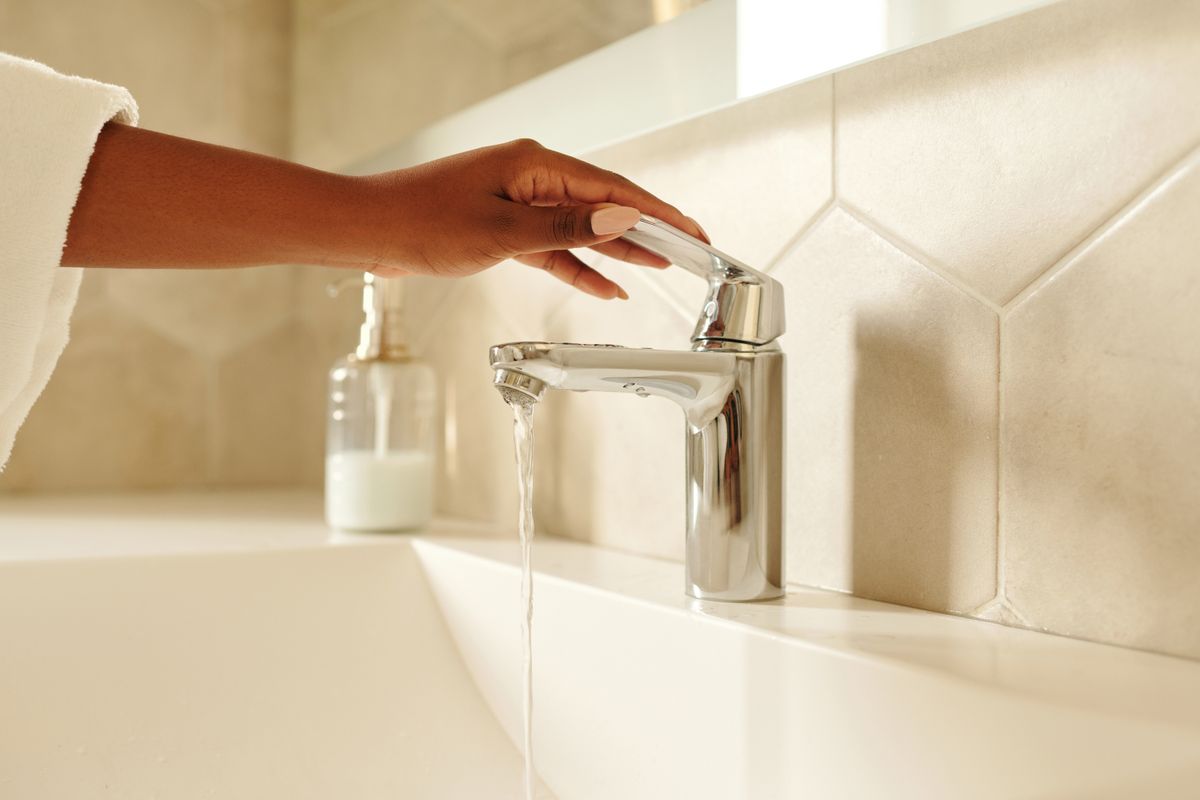 Hand turning a chrome bathroom faucet with water flowing, the simple fixture test that separates a whole-house pressure problem from a softener restriction