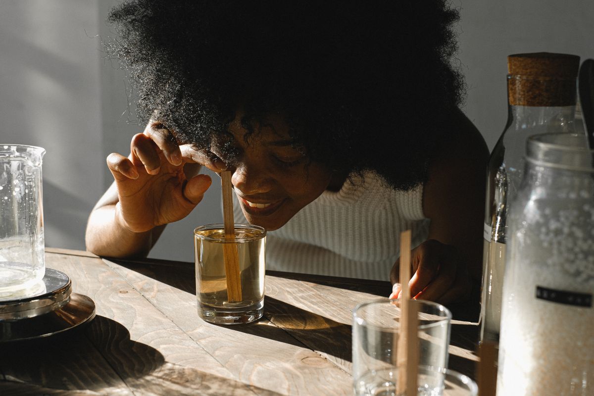 Woman holding a glass of water up to smell it in a sunlit room, the sniff test that separates hot-tap anode odour from sulfur coming from the well