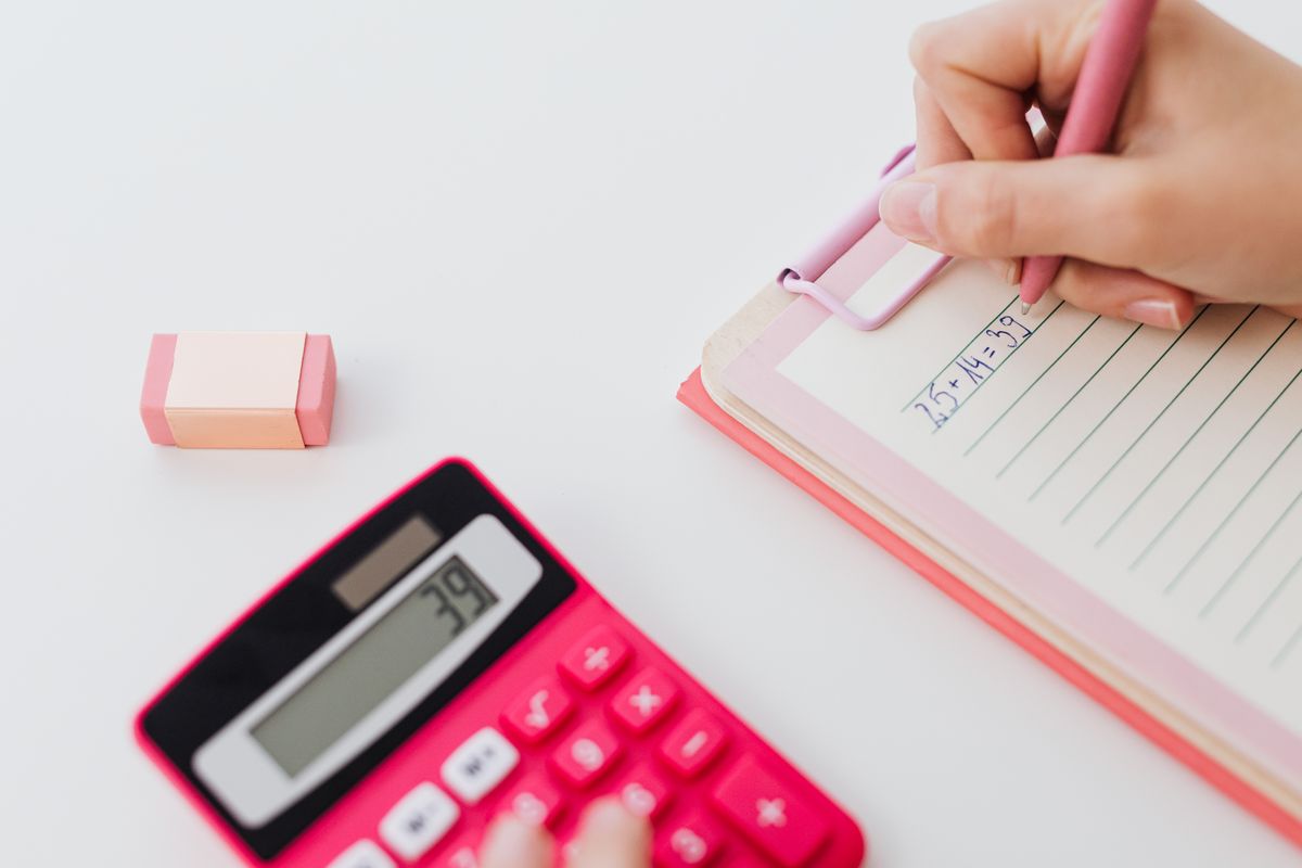 Hand writing a conversion in a notebook beside a calculator, converting a water hardness reading from ppm to grains per gallon