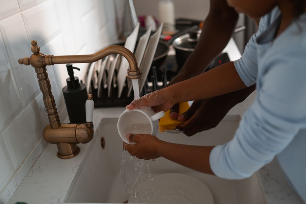 A child and an adult washing dishes together at a kitchen sink, part of the daily water use a family of four's softener is sized for