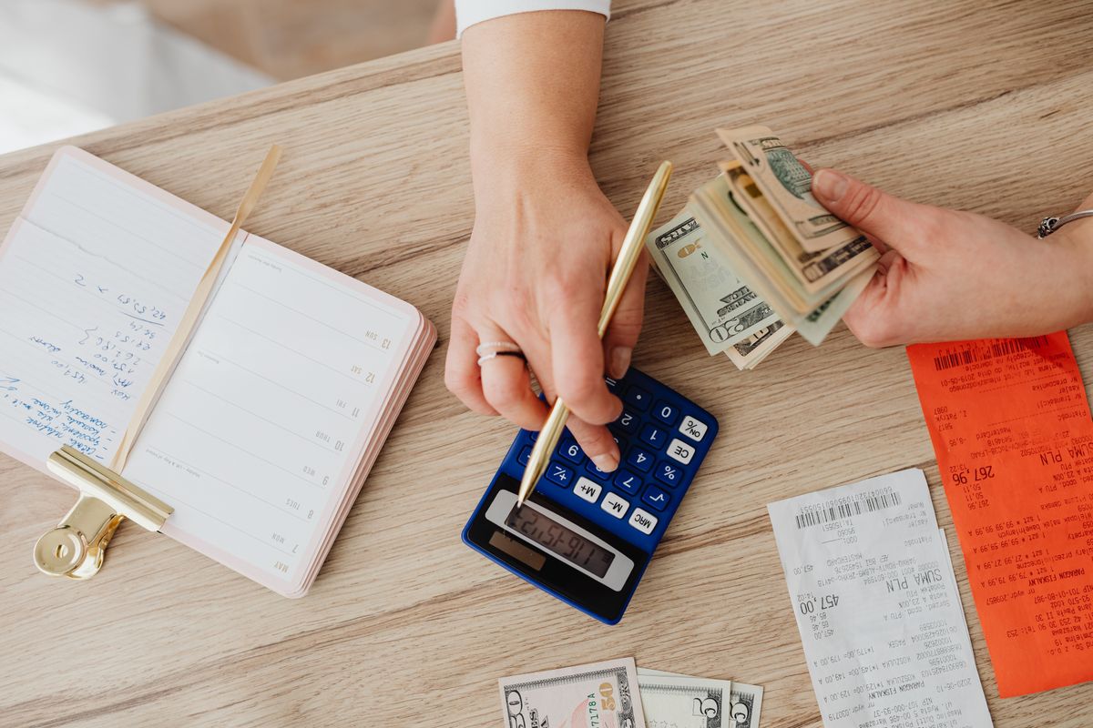 Hands writing household figures next to a blue calculator, cash and paper receipts, the salt and water bills that decide whether a Kinetico water softener pays back