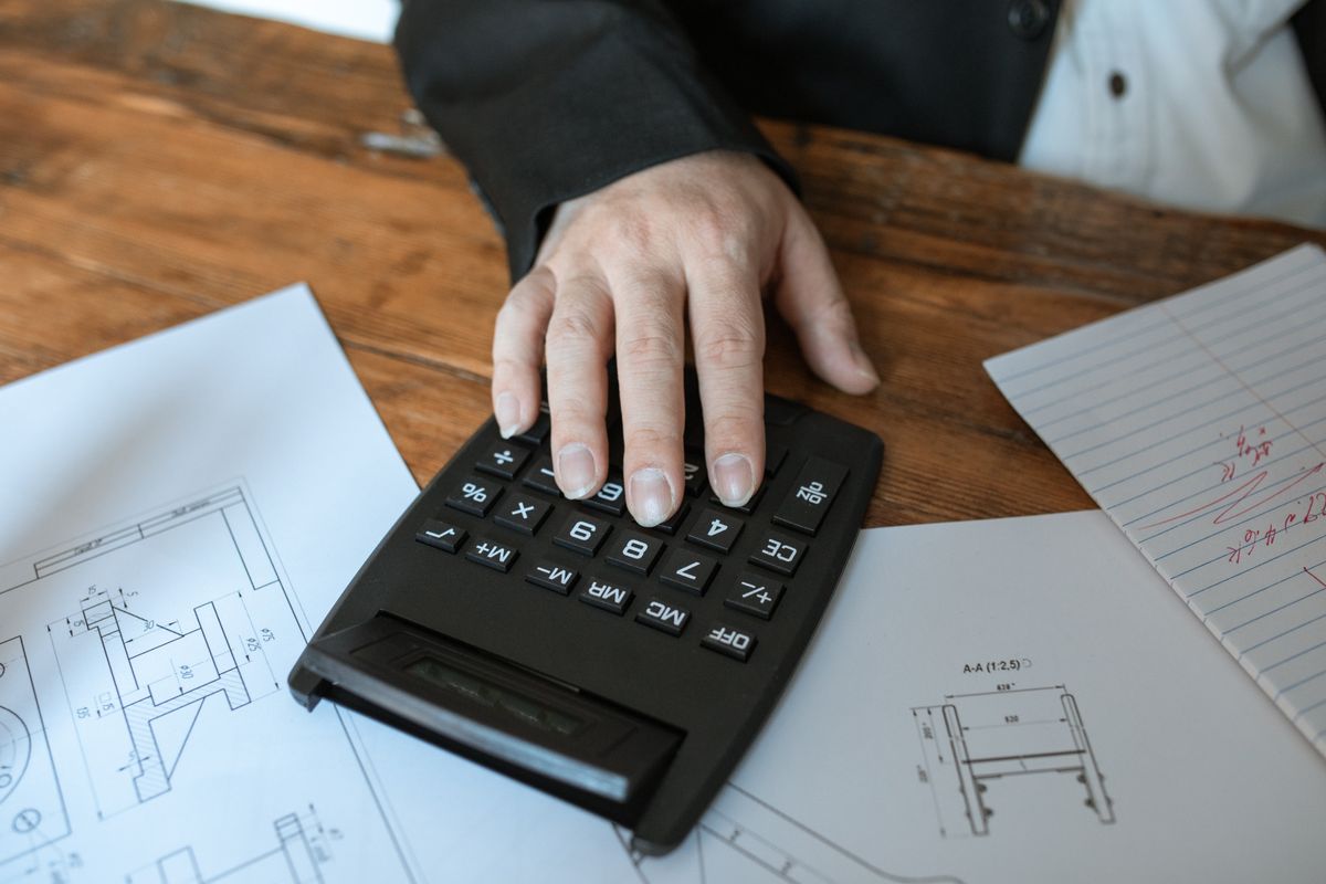 Hand working a desk calculator over printed technical drawings, the arithmetic that turns a well's iron result into a softener size