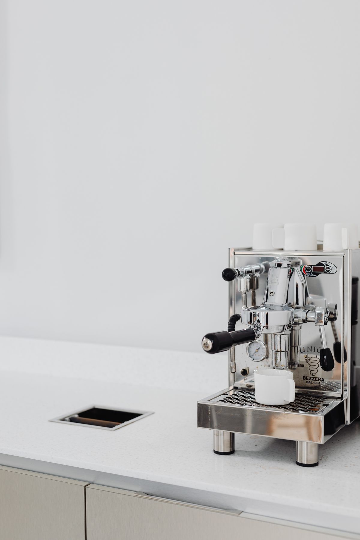 Stainless steel home espresso machine on a white kitchen counter with cups warming on top