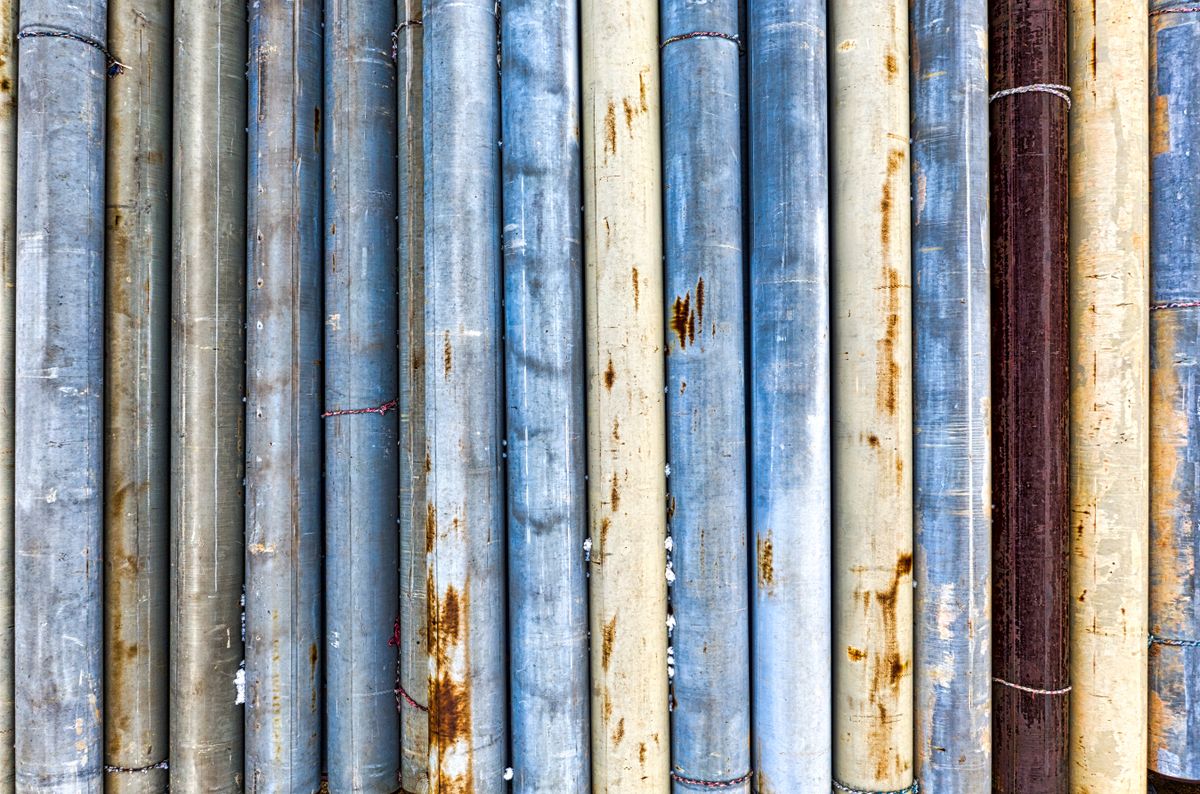 Lengths of galvanized steel pipe lined up side by side, several with rust bleeding through the worn zinc coating