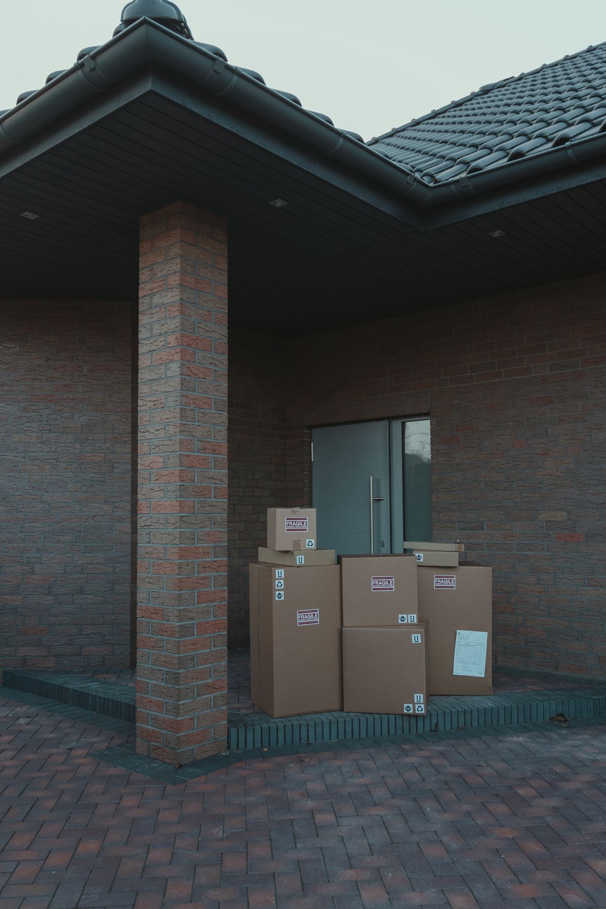 Stack of large cardboard shipping boxes at the entrance of a brick house, how an online water softener and brine tank arrive before a plumber installs them