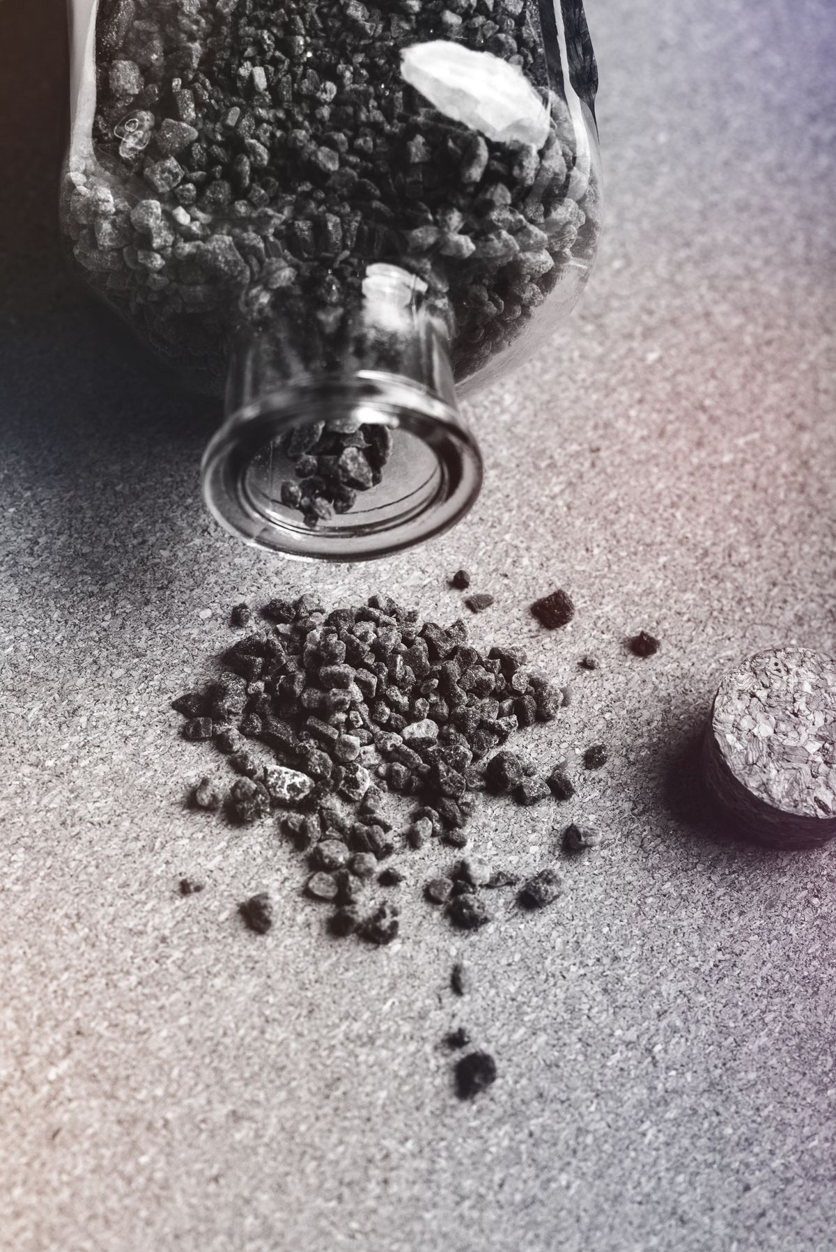 Dark granules spilled from a glass jar onto a table, resembling the black specks that appear in water after a softener