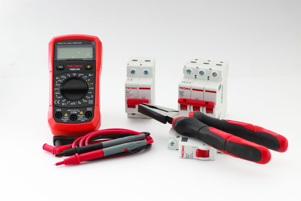 Digital multimeter lying beside electrical tools and circuit breakers, the kind of basic test gear used to confirm power before resetting a softener control