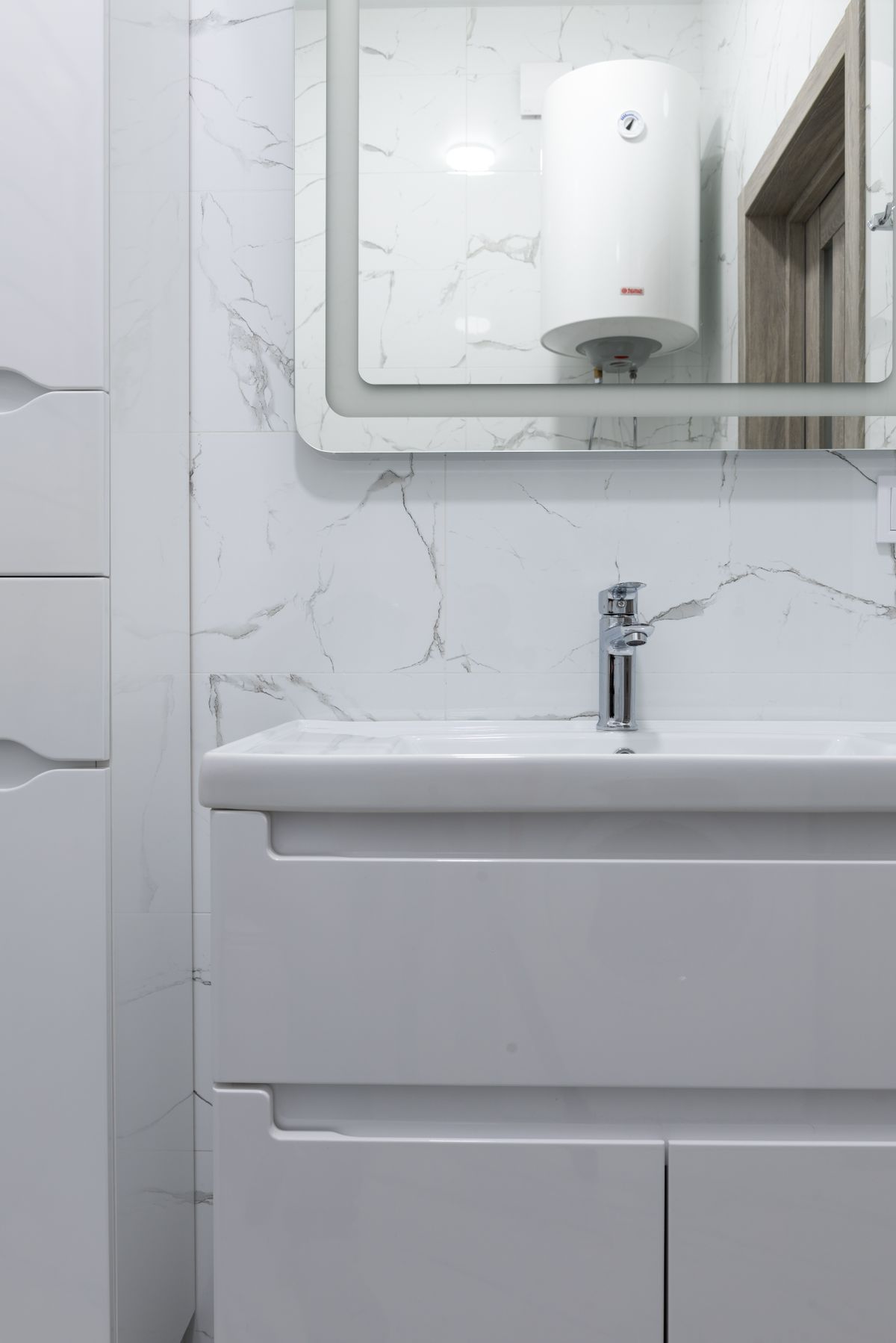Bathroom washbasin and faucet with a wall-mounted water heater reflected in the mirror above