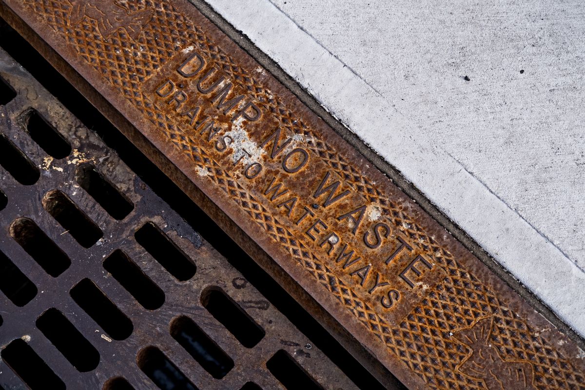Rusty storm drain grate cast with the words dump no waste, drains to waterways, the reason a water softener drain must not go to a storm sewer