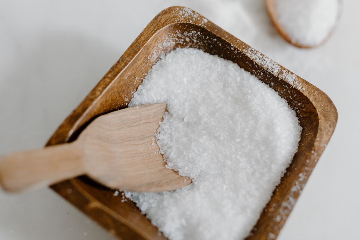 Coarse sea salt crystals in a wooden bowl with a small wooden scoop, the grade difference that determines how much insoluble material ends up on a brine tank floor