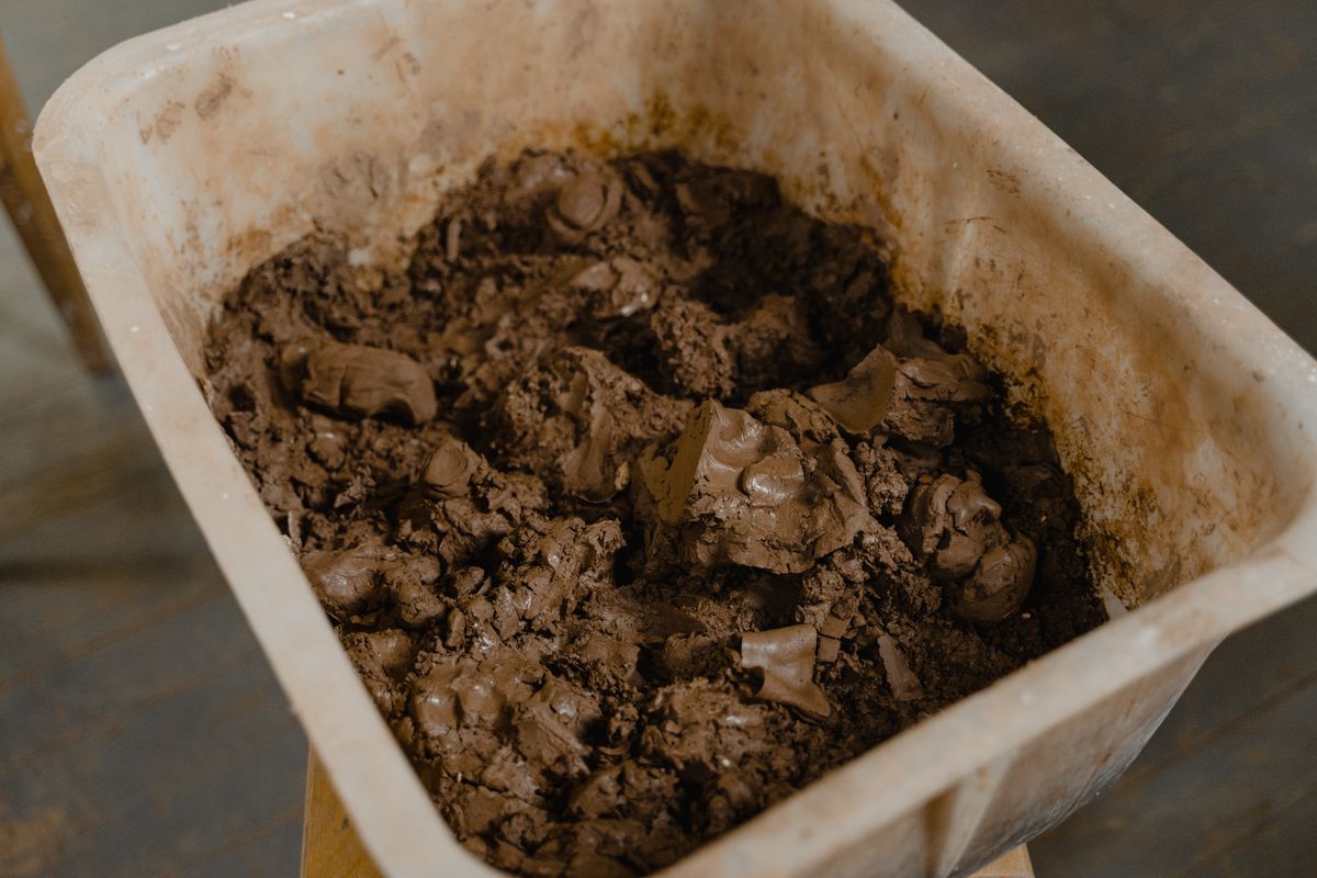 Wet grey clay sitting in the bottom of a large plastic container, closely resembling the recrystallised salt sludge that forms as mushing in a brine tank