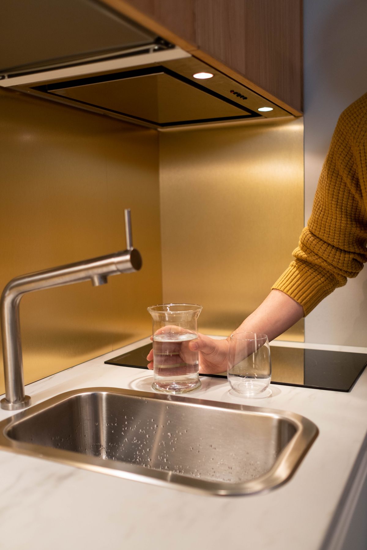 Person filling a drinking glass at a modern kitchen sink for a water hardness sample
