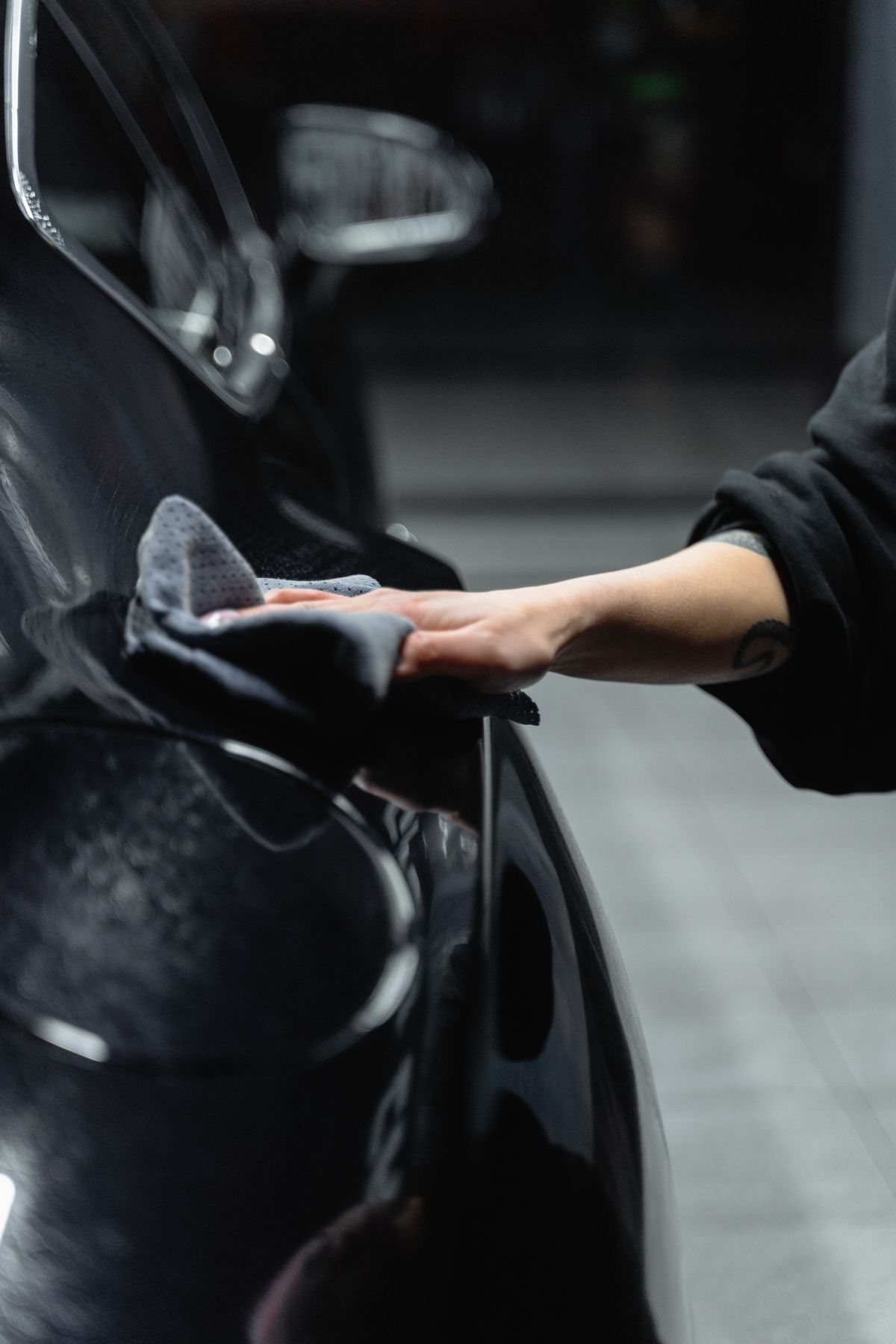 Hand wiping a shiny black car with a microfiber cloth to dry it before hard water spots can form