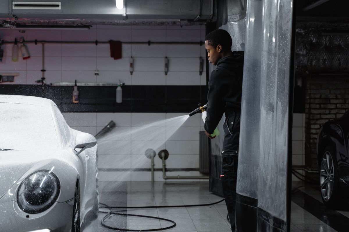 Man washing a white car with a pressure washer hose, the rinse water that leaves hard water spots on car paint as it dries