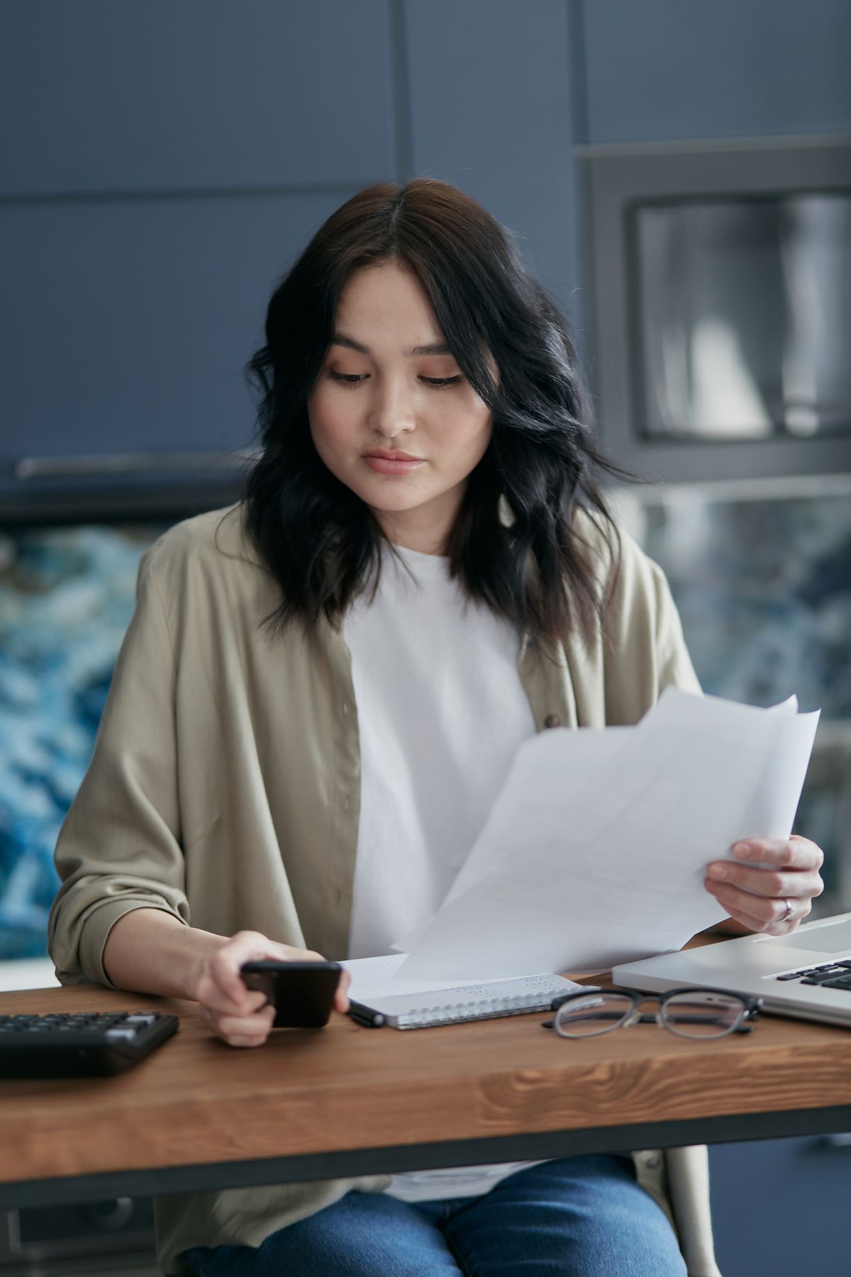 Homeowner reading through printed pages beside a calculator, laptop and phone, checking the line items of a Culligan water softener quote