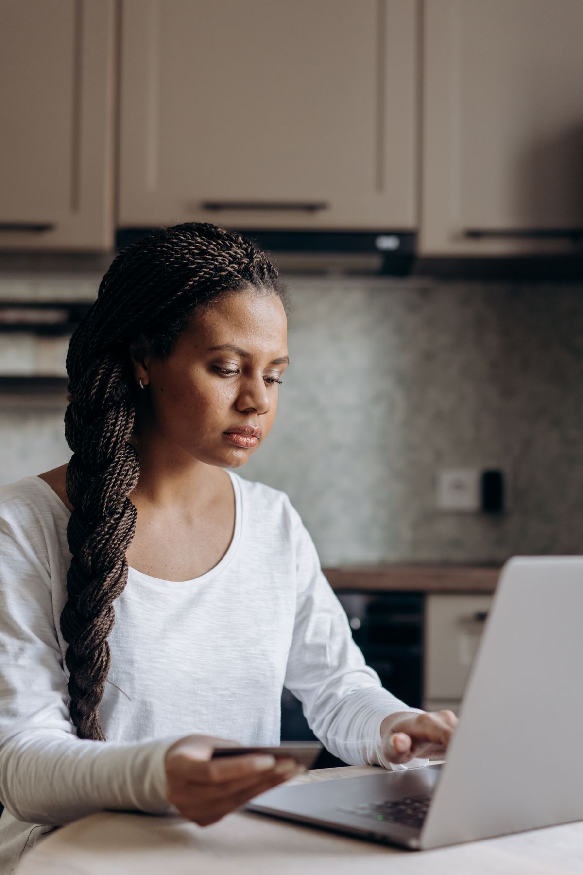 Woman holding a bank card while shopping online at a laptop in her kitchen, comparing where to buy a water softener