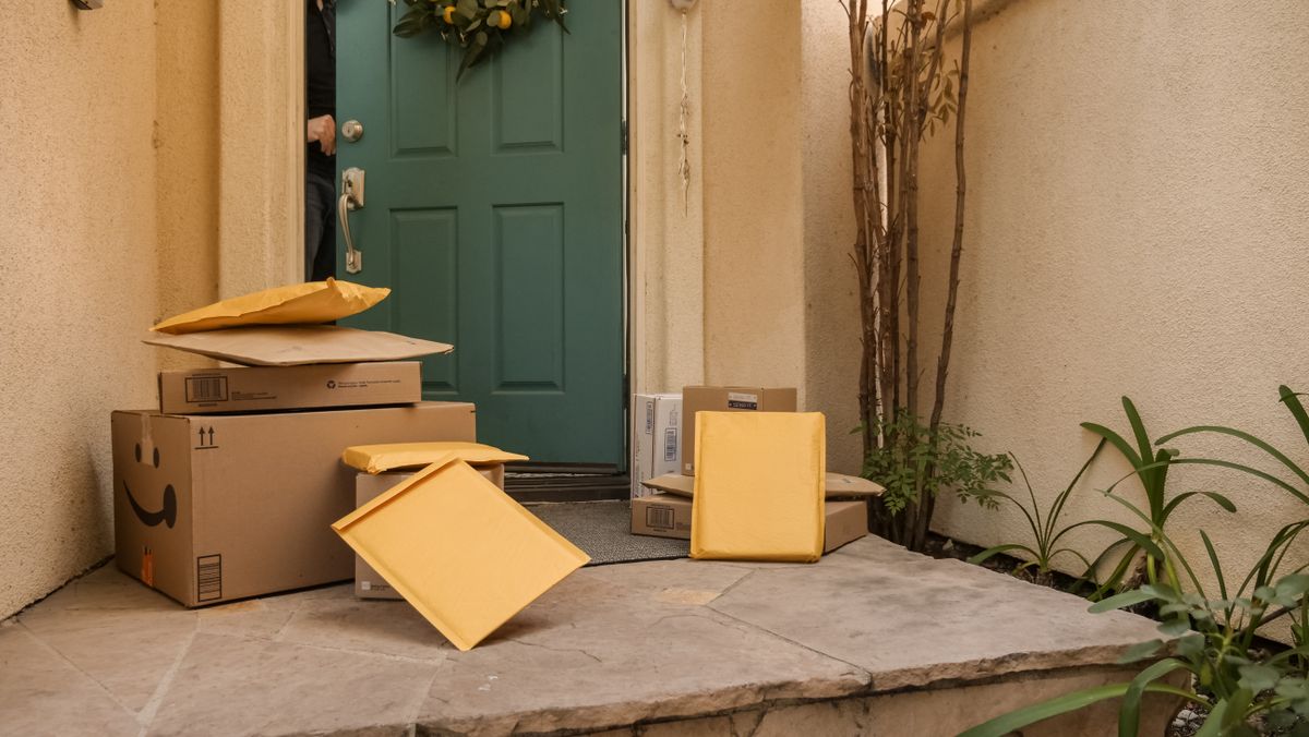 Stack of delivered cardboard parcels outside a teal front door, the way direct-to-home softener brands such as SpringWell and Pelican ship their systems