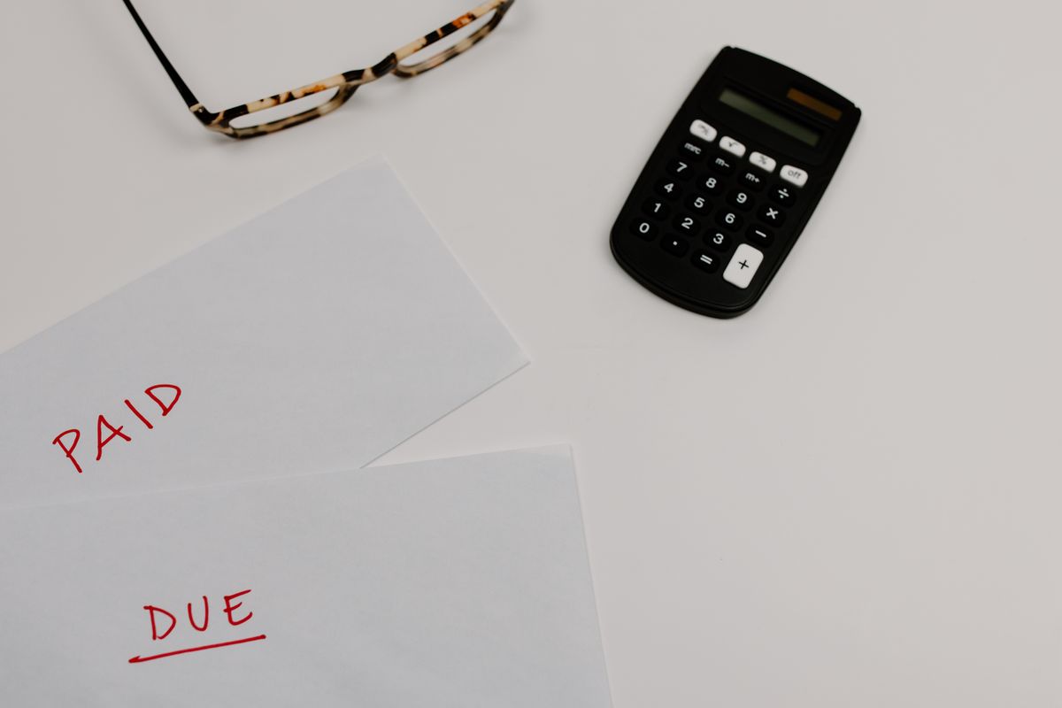 Envelopes marked paid and due beside a calculator and reading glasses, representing the payback worksheet for a whole house water softener
