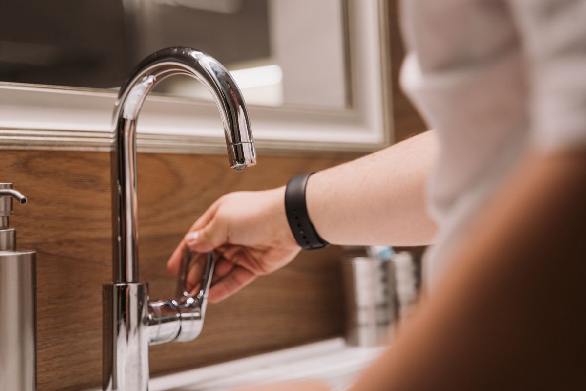 Hand turning on a chrome kitchen faucet, the tap where a combined softener and filter like the Hague WaterMax has to deliver soft, clean-tasting water