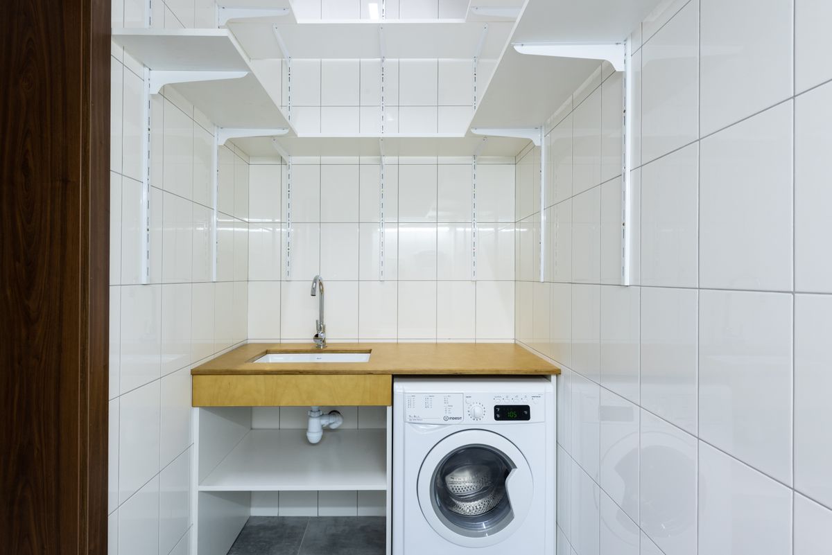 Small tiled laundry alcove with a front-loading washer, a utility sink and wall shelves, a closet-sized space where a compact softener can share the drain