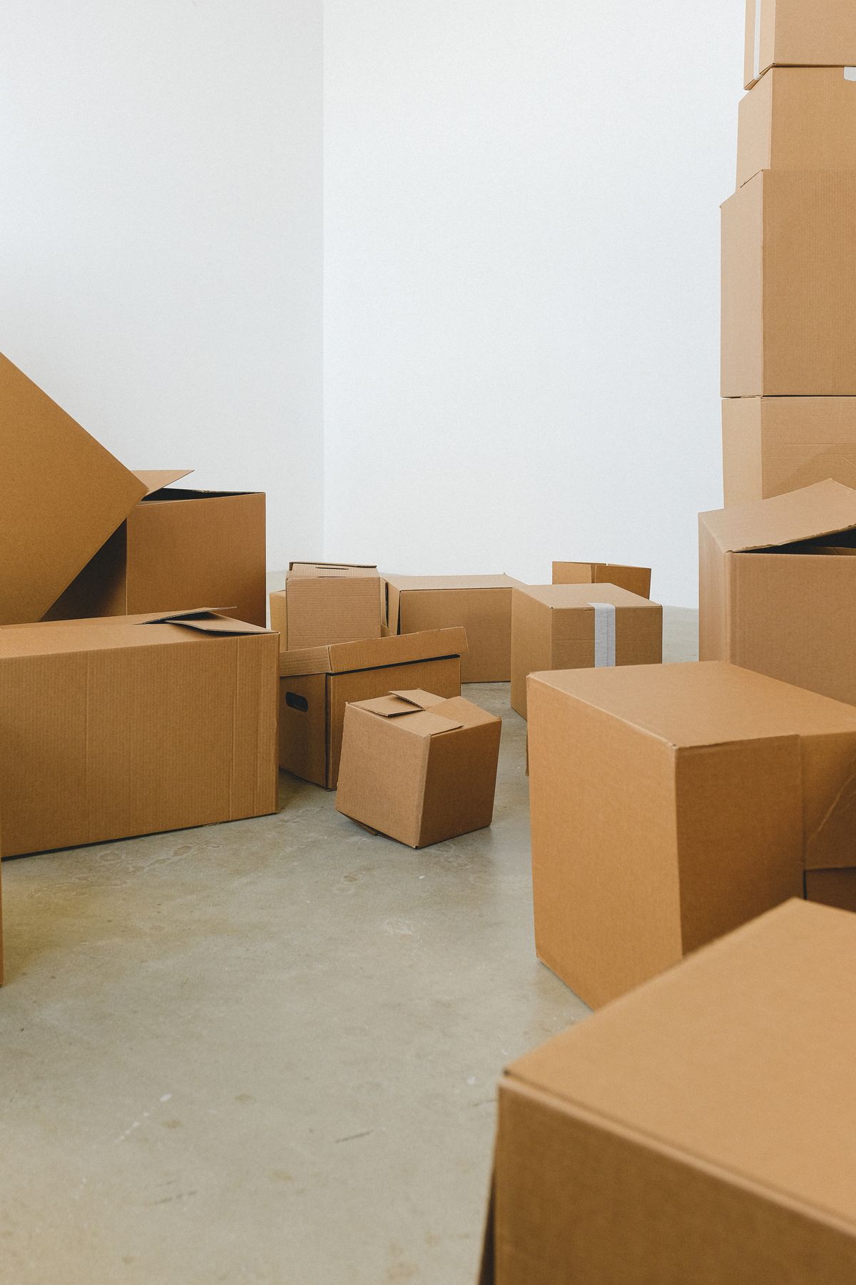 Sealed and open cardboard moving boxes stacked across the bare concrete floor of an empty room, mid-way through a house move