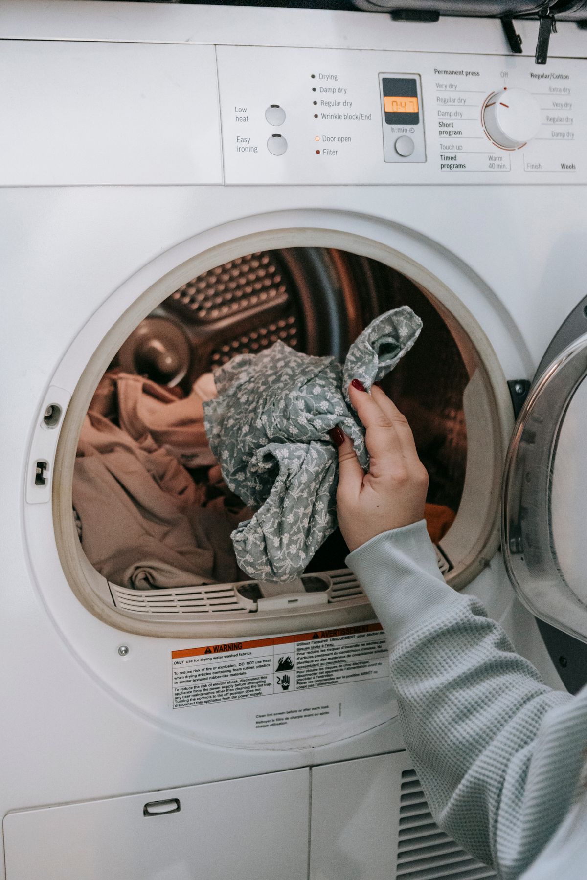 Woman loading a front-loading washing machine with laundry, one of the fixtures that runs alongside showers at a home's busiest moment of water use