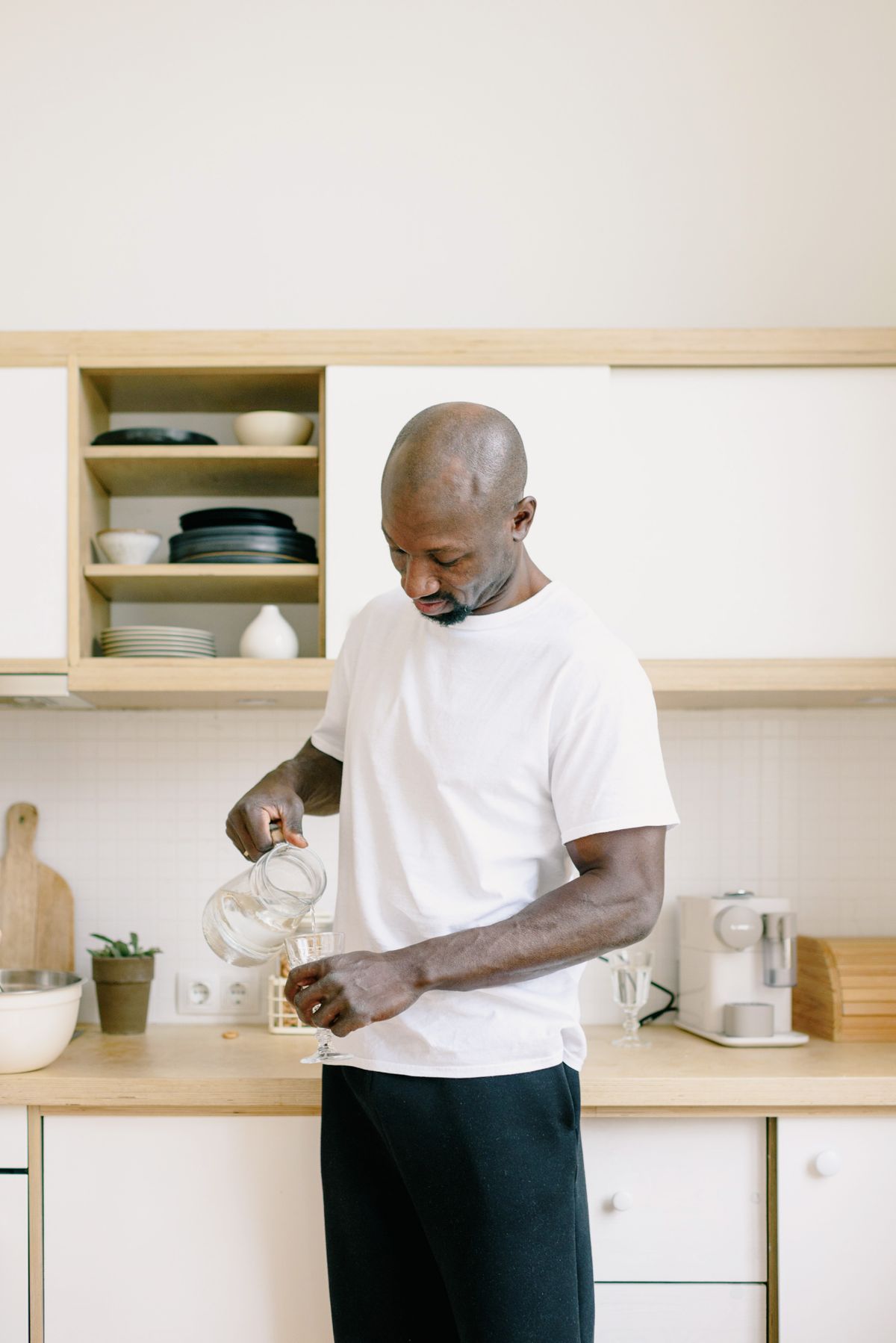 Man pouring water from a glass carafe into a drinking glass at a light wood kitchen counter
