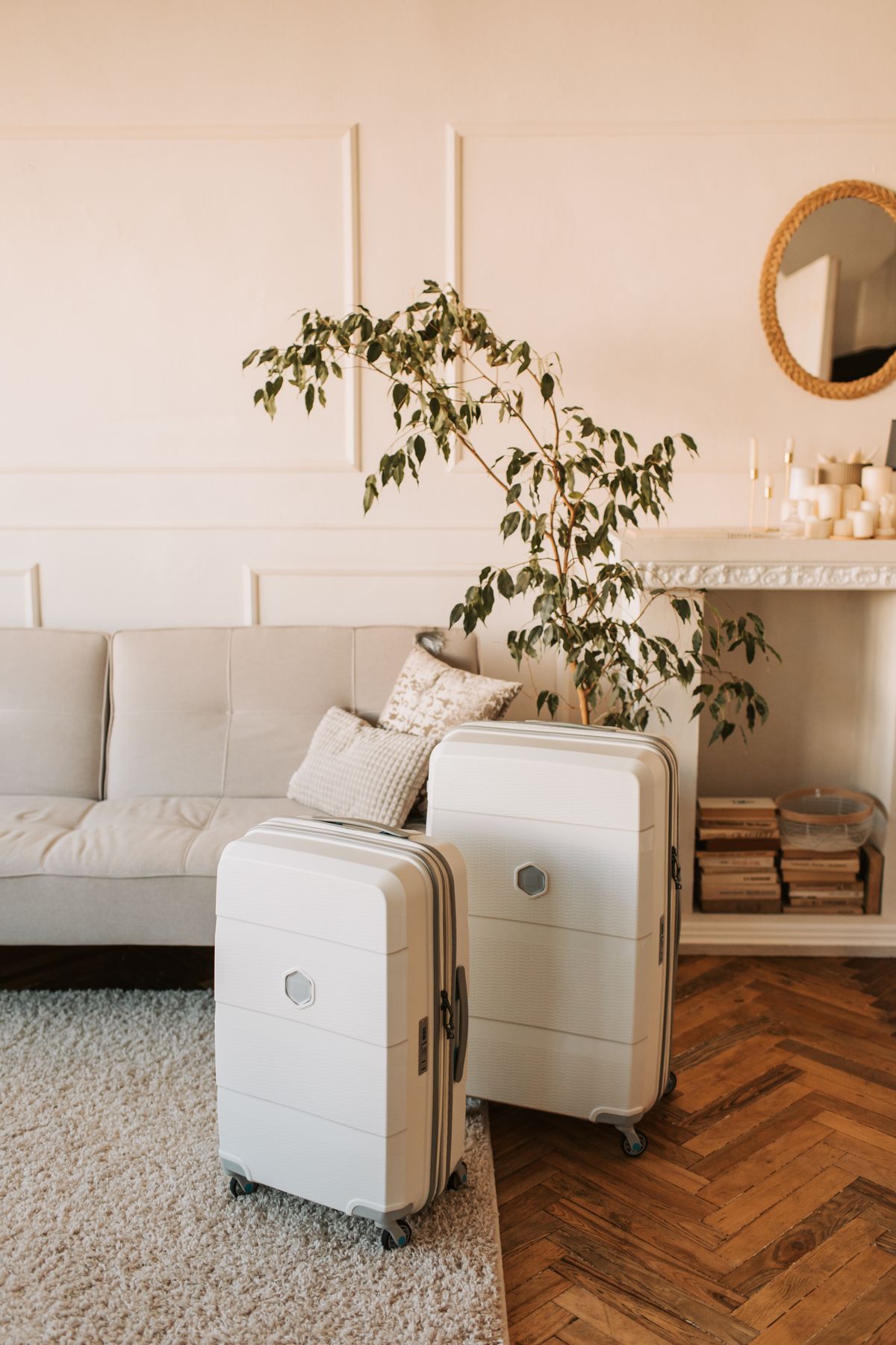 Two white hard-shell suitcases packed and standing in a living room beside a sofa and a potted plant
