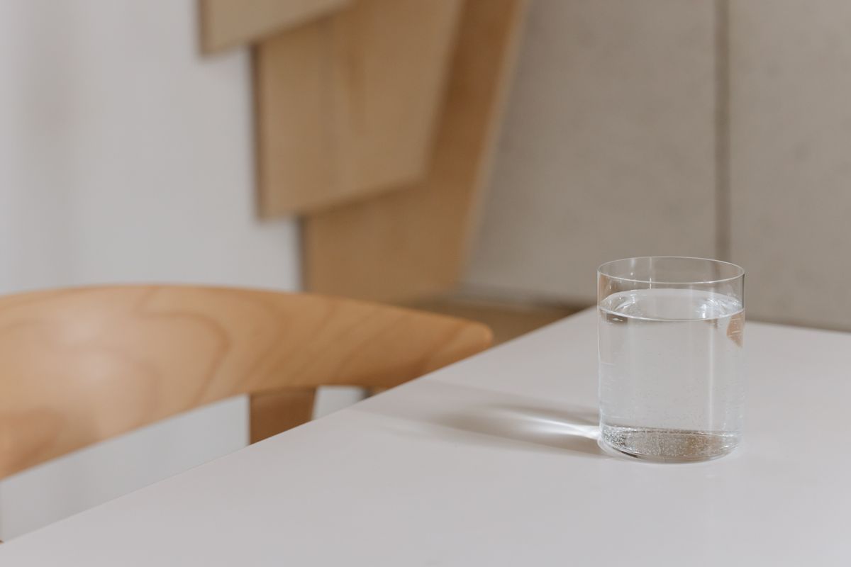 Single clear glass of water standing on a white table in soft daylight, the simple setup for a timed iron glass test