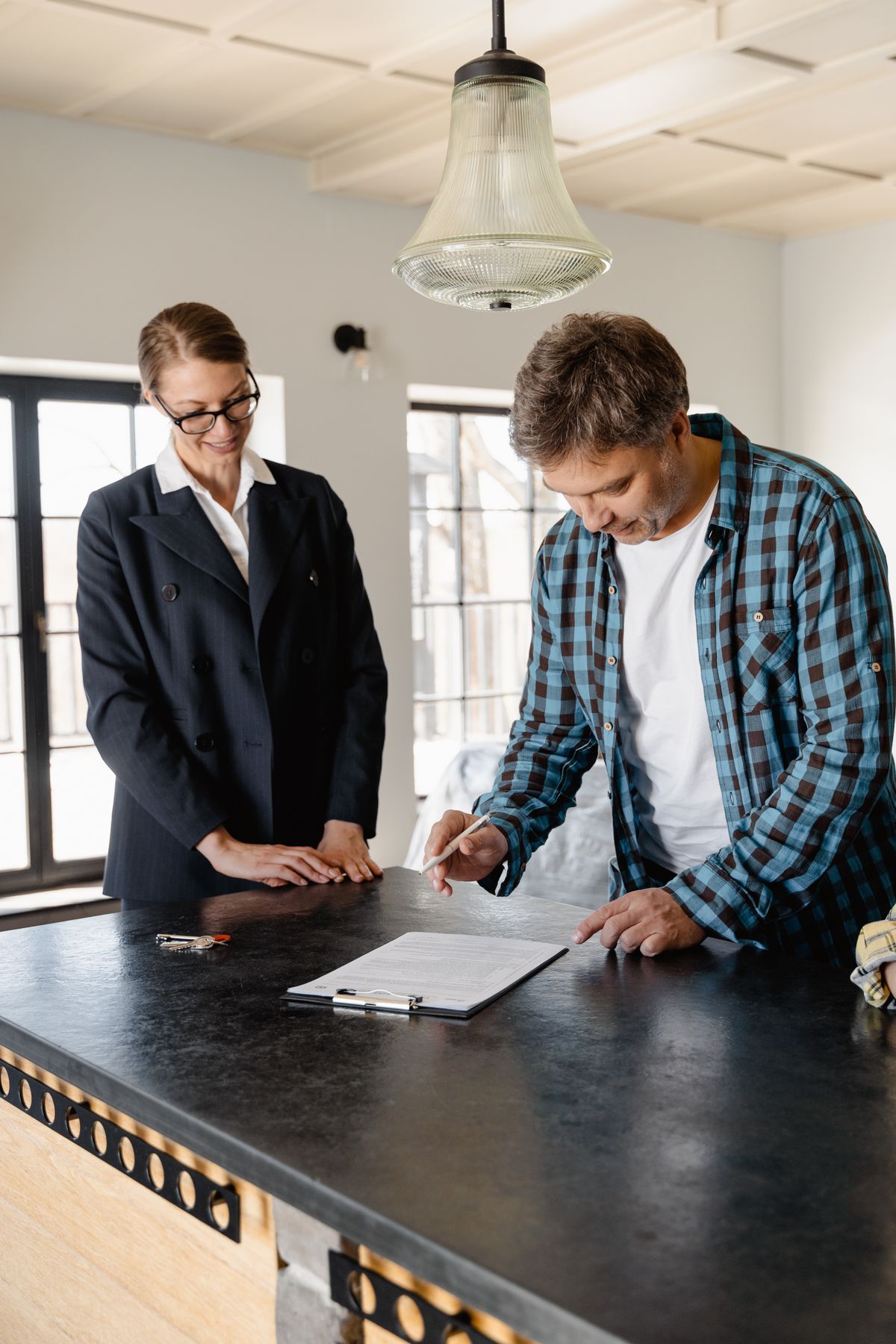 Homeowner in a checked shirt signing a clipboard at a kitchen island while a sales consultant watches, the in-home moment a Culligan water softener quote gets signed