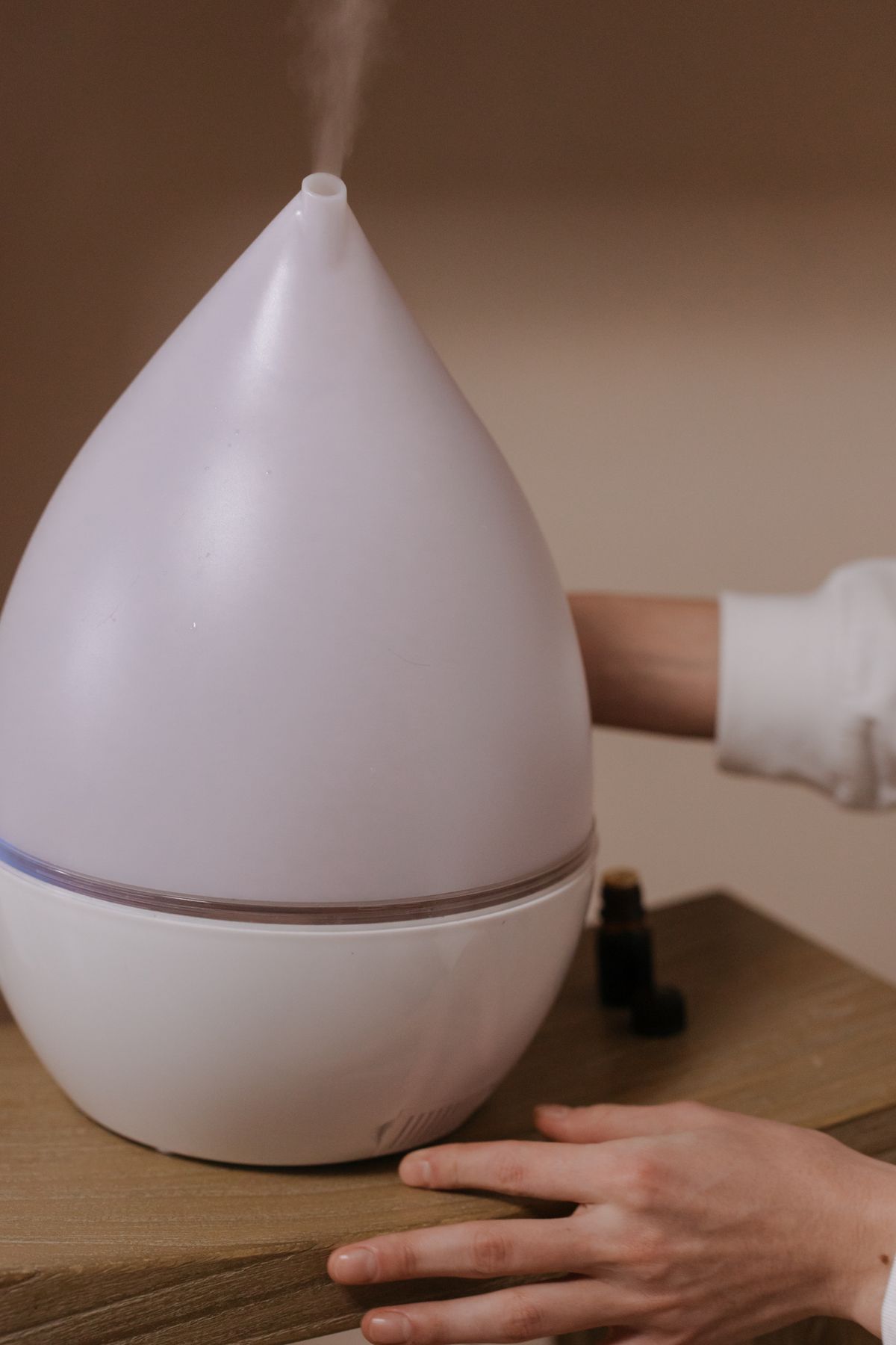 Modern ultrasonic humidifier emitting mist on a wooden surface indoors, the source of humidifier white dust