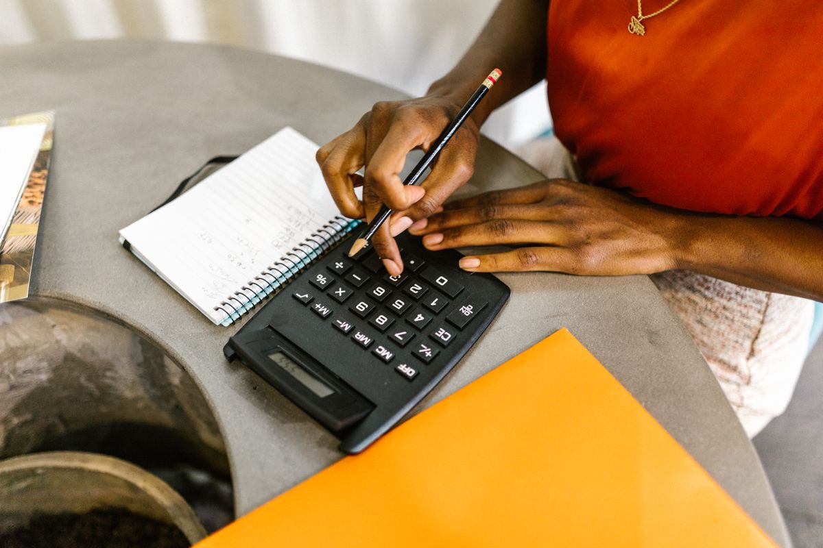 Person using a calculator and pencil beside a spiral notepad while working through numbers at a table