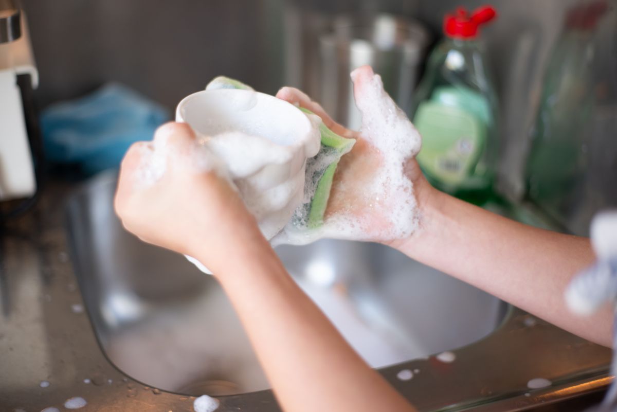 Hands washing a mug under a running kitchen tap, one of the fixtures counted in a family of four's busiest moment of water use
