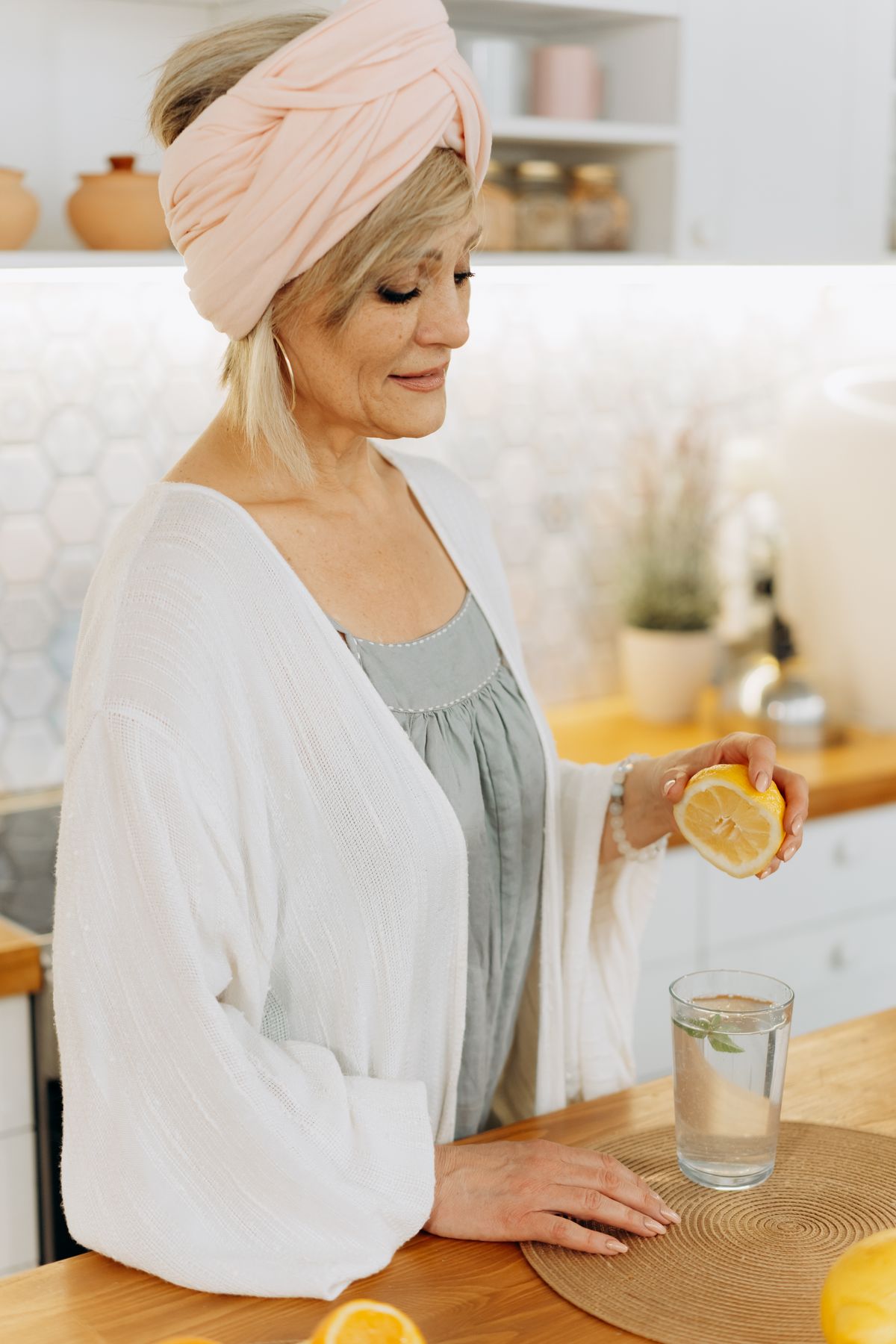 Senior woman squeezing a lemon into a glass of water in a home kitchen, drinking water for a household on a low-sodium diet