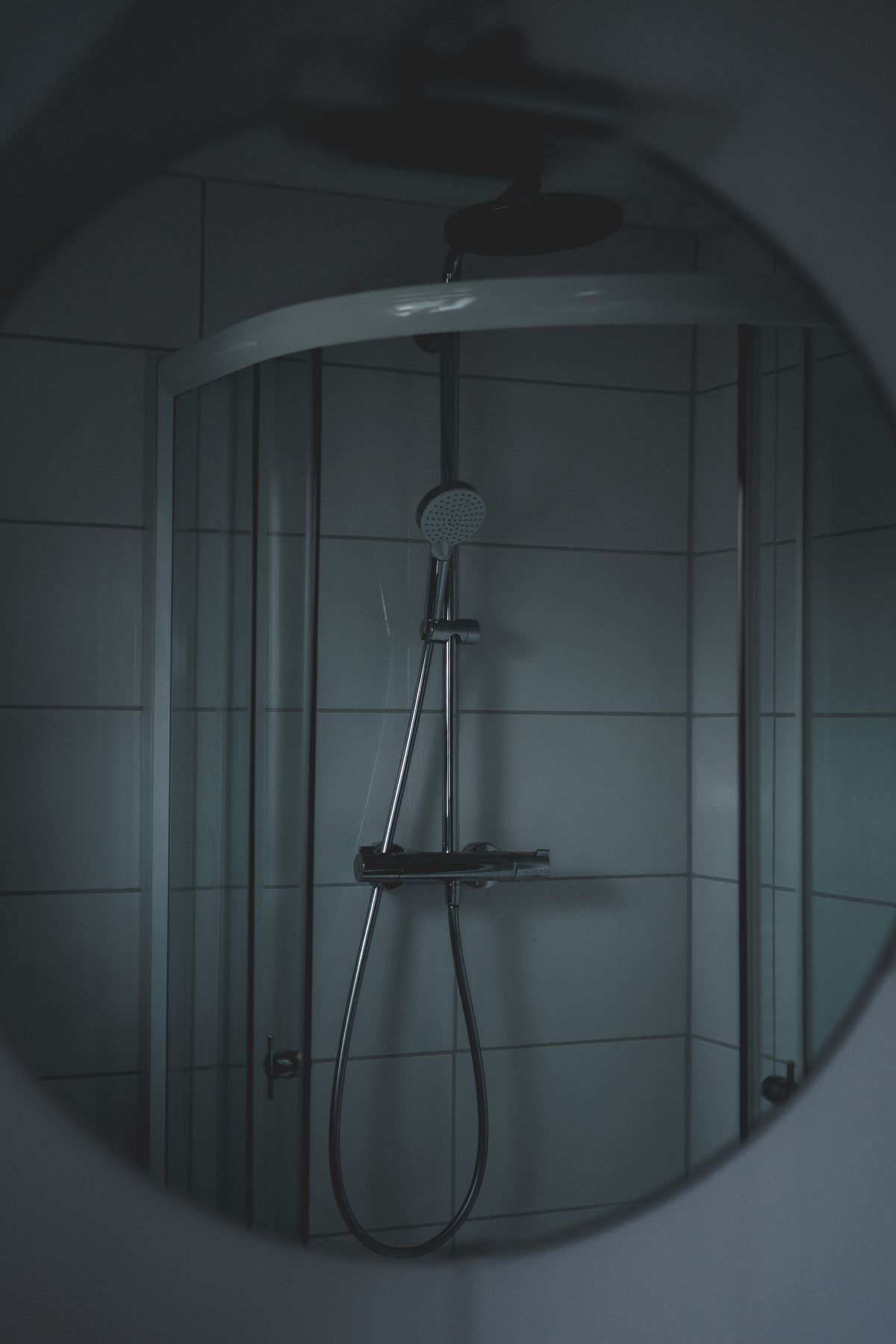 Glass shower enclosure with a chrome thermostatic mixer and hand shower, reflected in a round mirror: the glass and fixtures where SpringWell FutureSoft or Nuvo H2O is meant to slow new scale