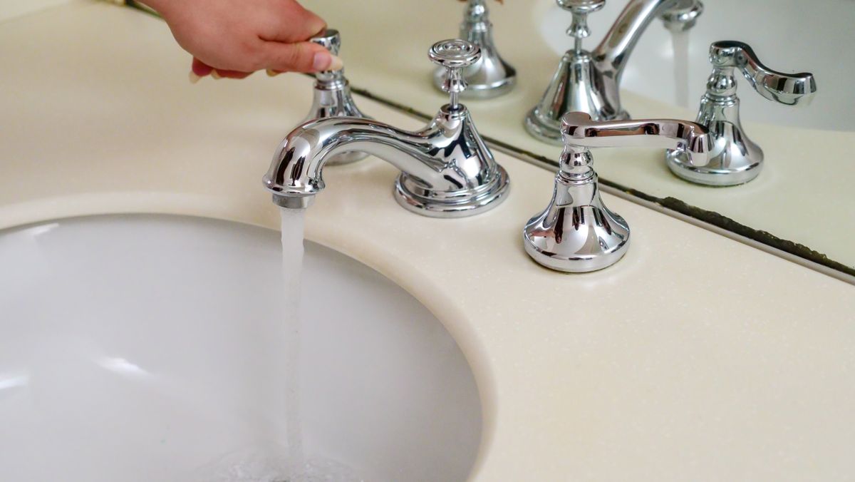 Hand operating a chrome bathroom faucet with running water, where scale on faucet aerator restricts flow