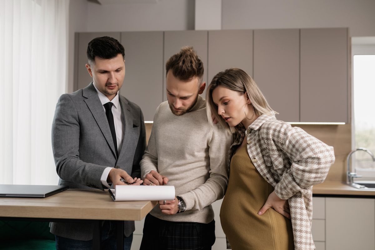 Couple standing with a sales consultant at a kitchen counter reviewing a document together, the in-home visit where an EcoWater dealer presents series and plan options