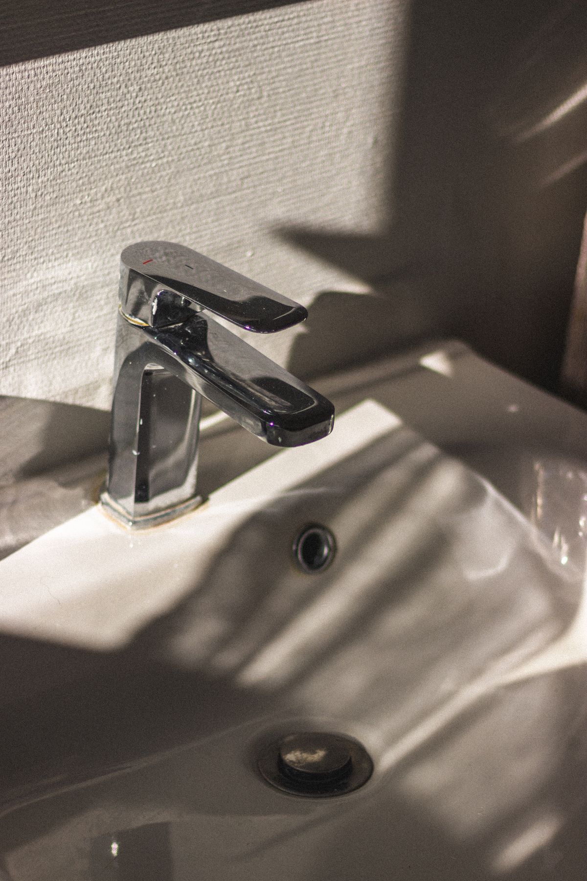 Chrome single-lever faucet over a white basin in sunlight, a fixture a whole-house salt-free water conditioner is bought to keep free of scale