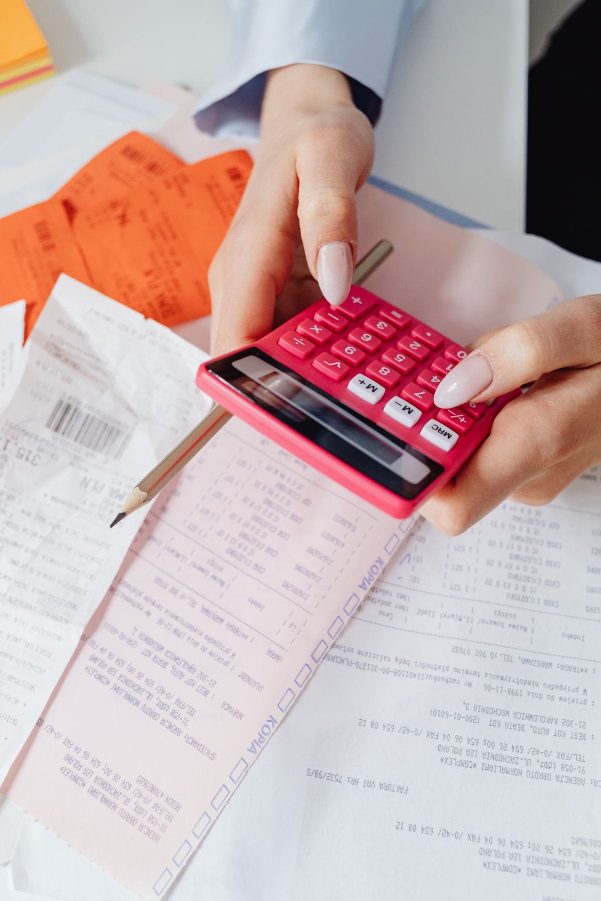 Hands using a red calculator over a stack of itemized receipts and invoices, the way to add up each line of two water softener quotes before choosing